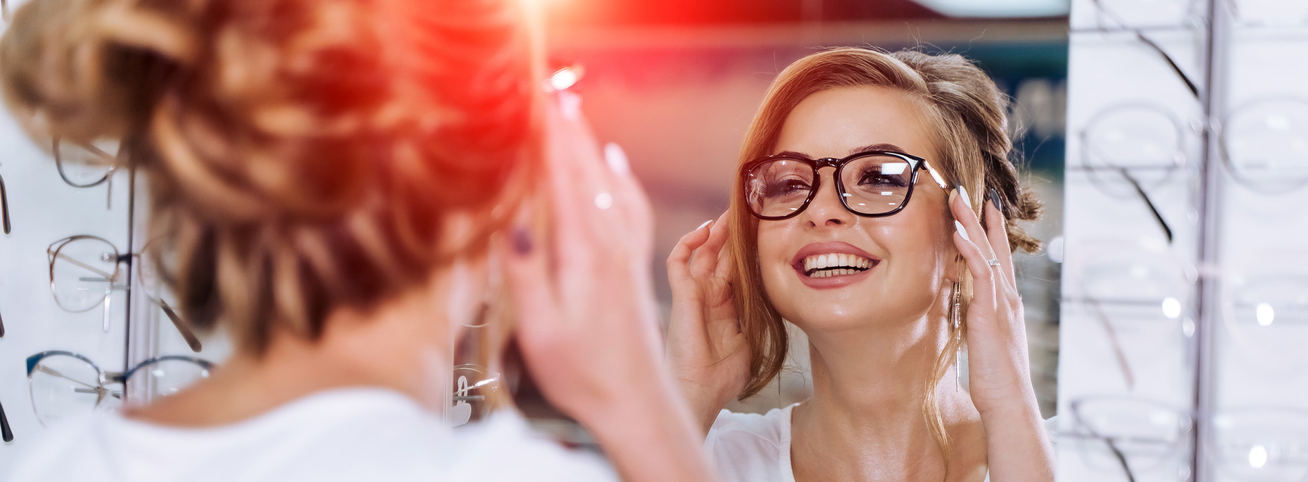 Woman applying makeup in front of mirror, smiling with eyes closed, in brightly lit room.