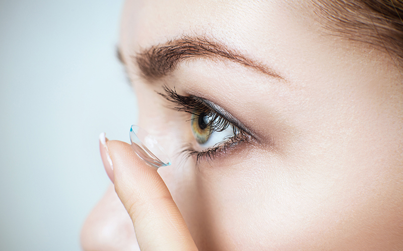 An adult female hand holding an eye examination tool, with a close-up view of her eye and eyelashes.
