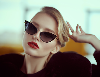 Woman in sunglasses with red lipstick, posing against a yellow background.