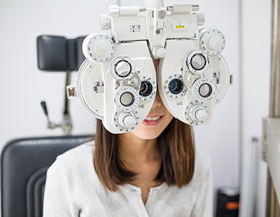 An individual wearing glasses and seated in an eye examination chair, with a focus on the eye chart in front of them.