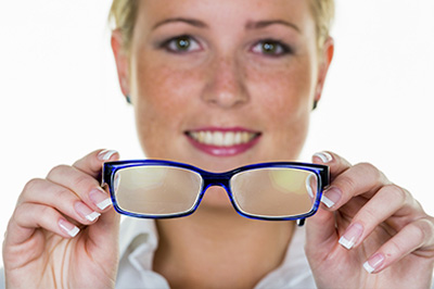 A woman wearing glasses holds them up to her face, showcasing the frame and lenses.