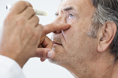 A man receiving a medical examination with an eye test, where a healthcare professional is holding a device near his eye.