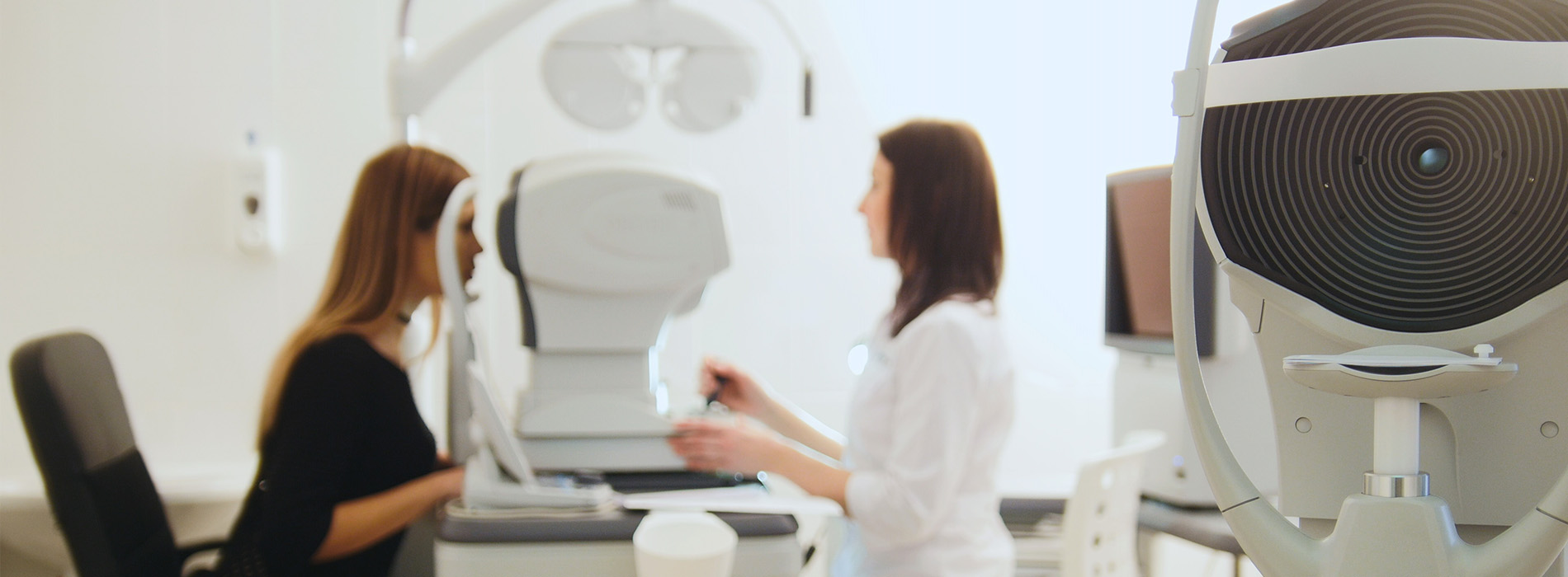 Two individuals in a modern optical equipment room, with one person seated at a desk and another standing, engaged in discussion or activity.