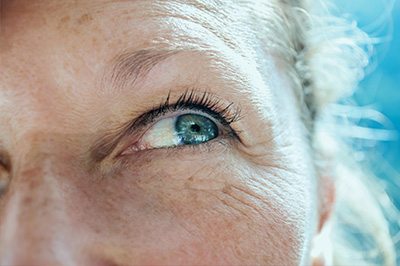 The image is a close-up photograph of an elderly person with light blue eyes, looking directly at the camera.