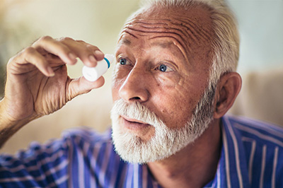 A man with a mustache and goatee, wearing glasses, is holding up a magnifying glass to inspect something closely.