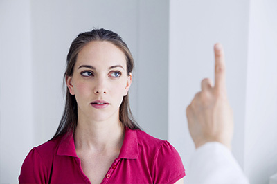 The image depicts a woman with her finger pointing upwards towards the camera, while a man in a white lab coat is seen from behind, looking at her.